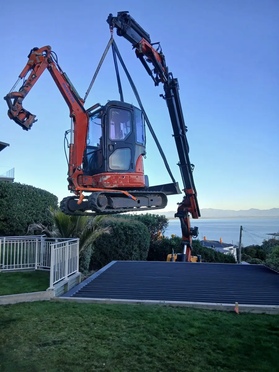 Excavator suspended mid-air during a crane lift-in on a tight coastal site