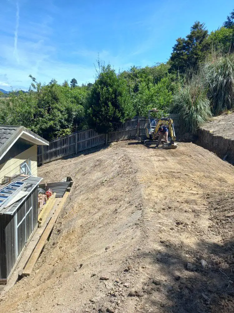 Excavator working a steep, boxed-in backyard right against a house
